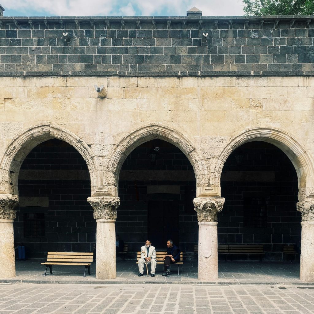 Course Two elderly men sitting quietly under a historic stone colonnade, offering a serene urban scene.